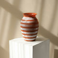 Orange and white striped glass vase on a display plinth