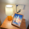 Orange ceramic table lamp with pleated shade illuminated on bedside table