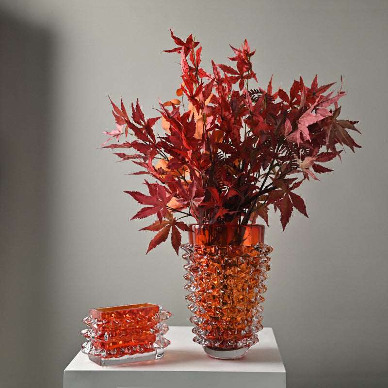 Orange and clear spiked glass vase with red autumn leaves