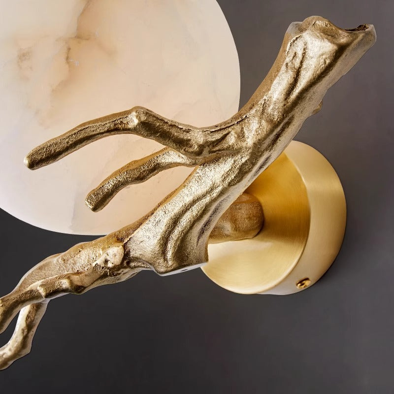 Close up texture detail of cast metal gold branch arm holding an alabaster-style glass shade