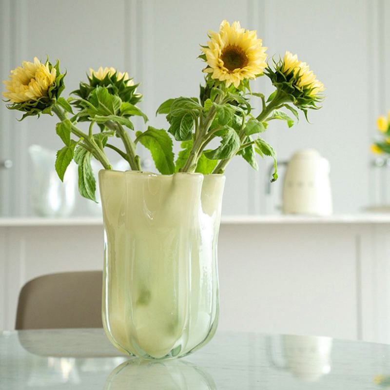 Pale green fluted glass vase with sunflowers on table