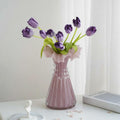 Pink fluted glass vase with purple tulips on table