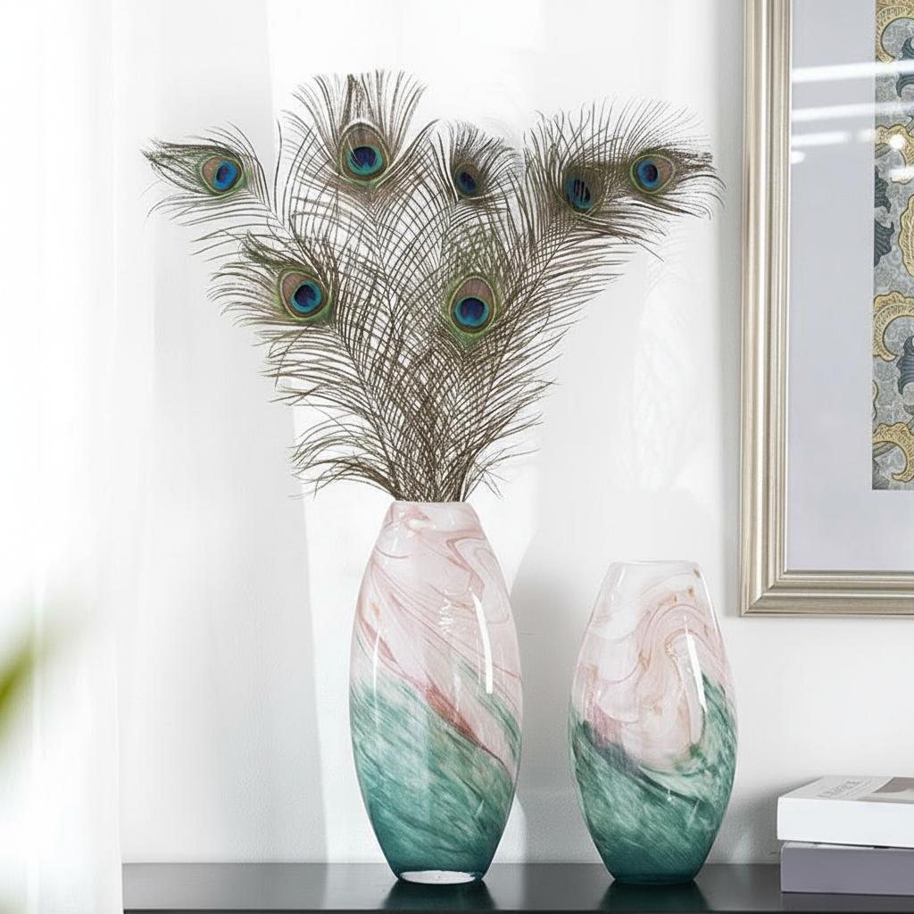 Two pink and teal marbled glass vases with peacock feathers on a console