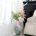 Large marbled glass vase with floral arrangement placed on the floor