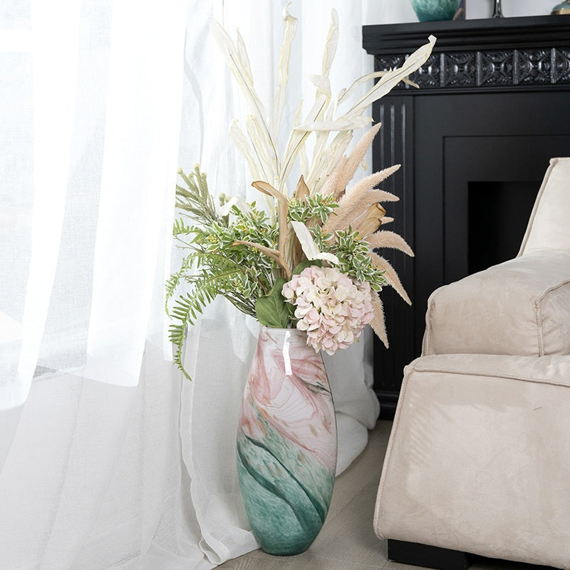 Large marbled glass vase with floral arrangement placed on the floor