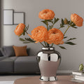 Polished silver urn vase with orange flowers on living room table