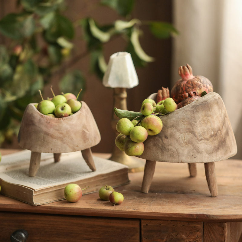 Two sculptural wooden tripod bowls styled with green apples and pomegranates on a rustic table