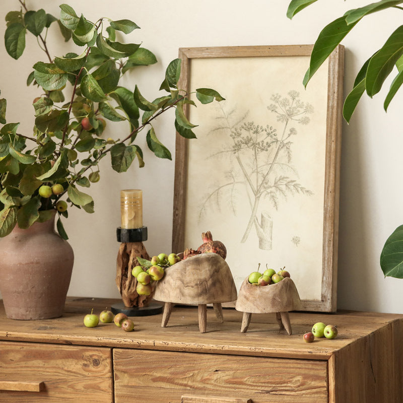 Lifestyle shot of hand-carved wooden fruit bowls on a sideboard with antique botanical prints and foliage
