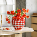 Porcelain globe vase with red apple pattern holding orange tulips on stone table