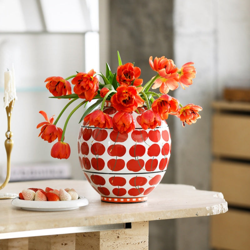 Porcelain globe vase with red apple pattern holding orange tulips on stone table