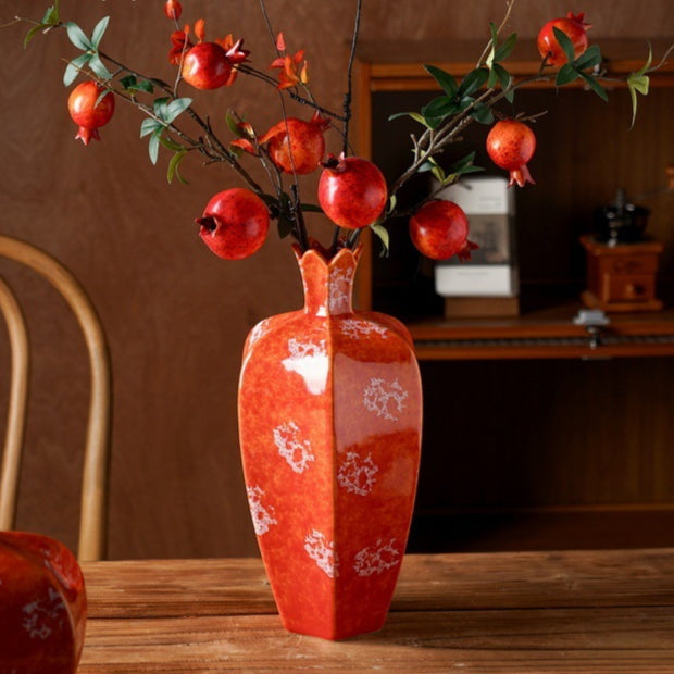 Tall red ceramic pomegranate vase with branches on table