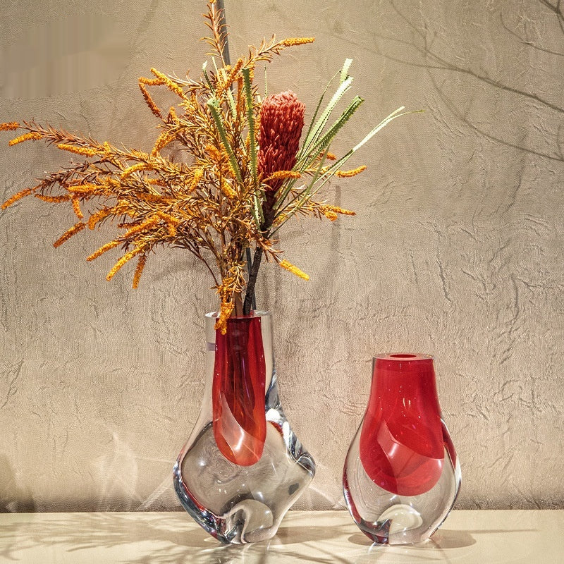 Artistic red and clear glass vases with floral arrangement against textured wall