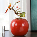 Red glazed ceramic apple sculpture with metal bird branch front view