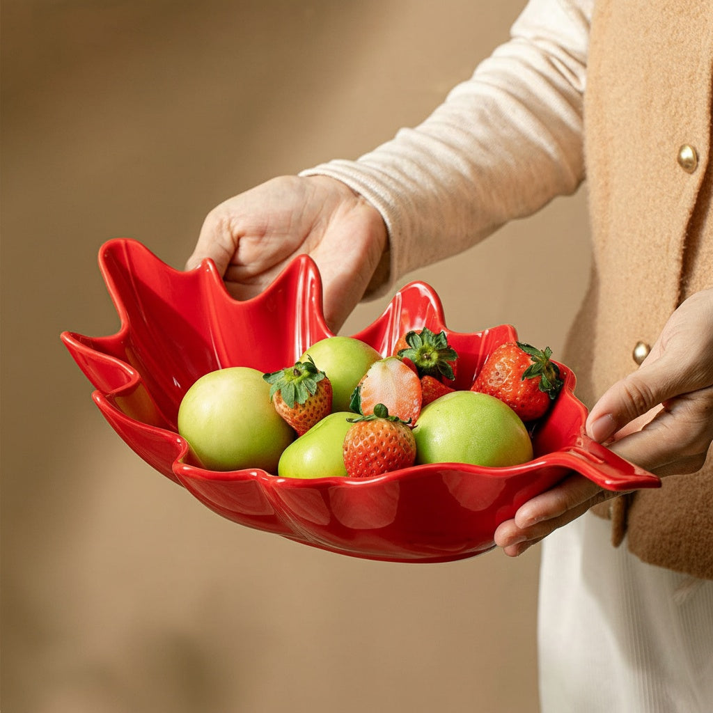 Person holding a red glazed ceramic leaf shaped bowl filled with fresh fruit