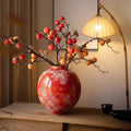 Red mottled glaze ceramic vase with persimmon branches on wooden table