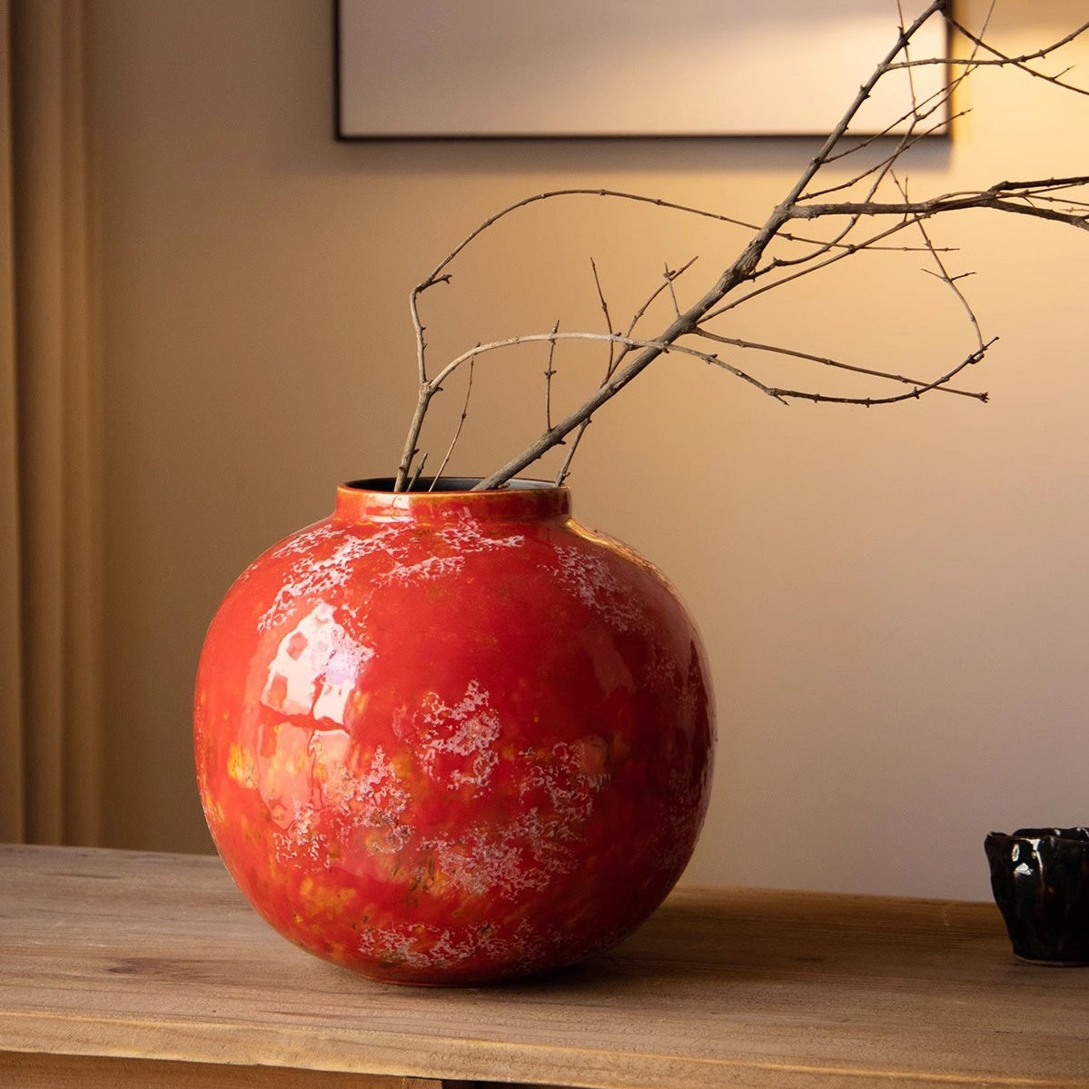 Close up of red textured ceramic vase with bare branches showing mottled finish