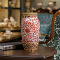 Red floral ceramic vase with gold finish metal accents on table