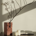 Red travertine stone vase with dried branches on table