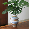 Ceramic table vase holding monstera leaves on wooden table