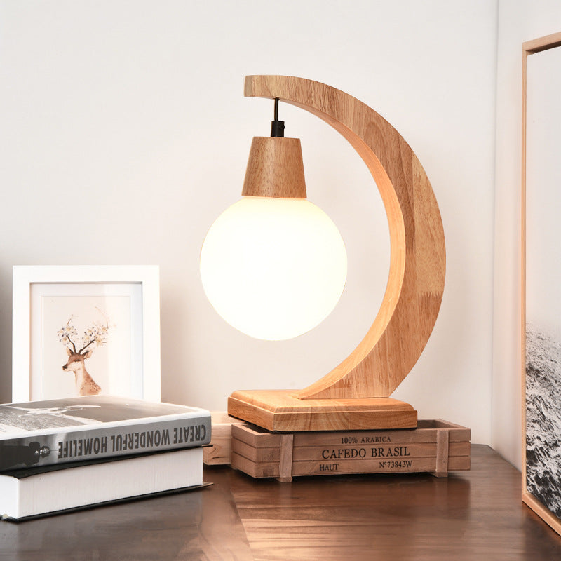 Front view of natural rubber wood crescent table lamp with lit glass globe