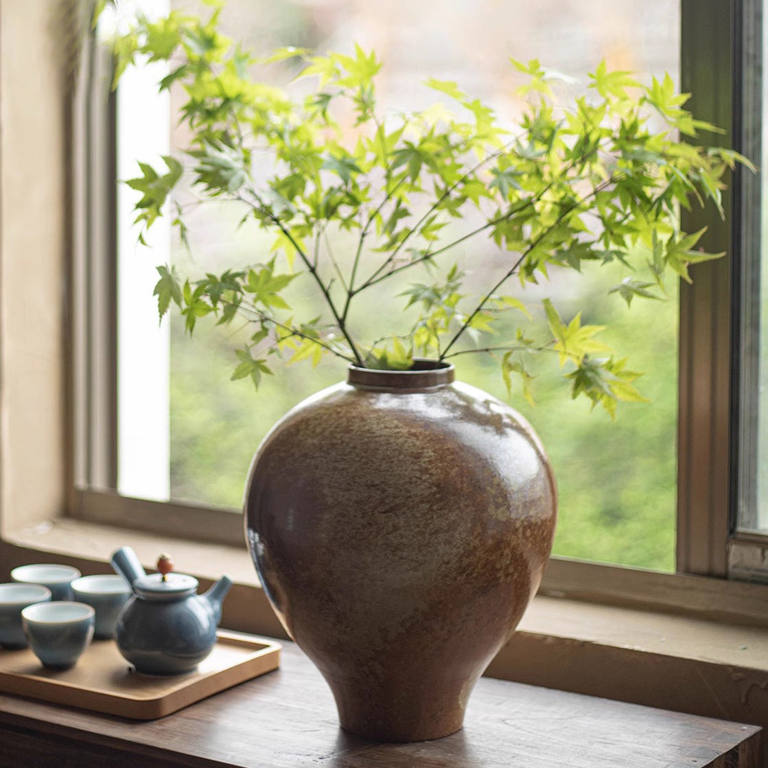 Rustic ceramic vase styled on a wooden surface by a window