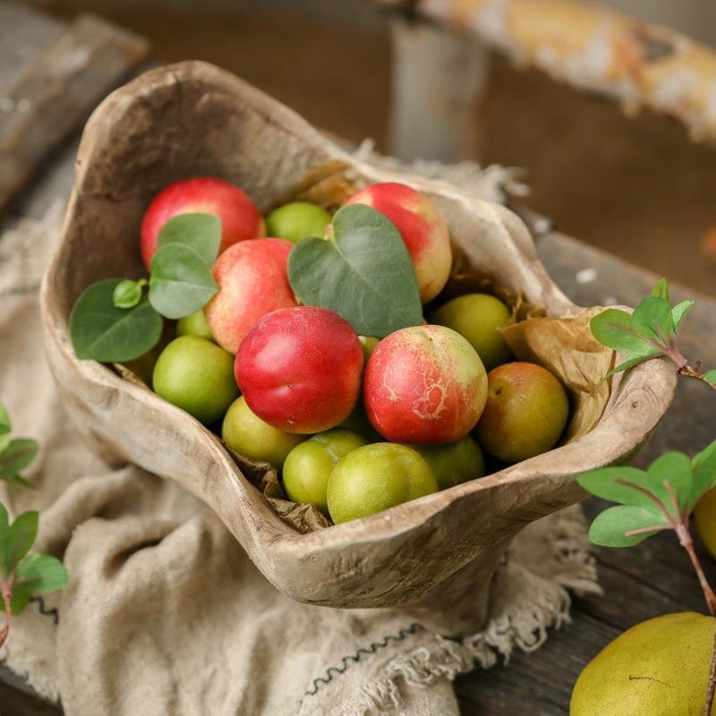Top down view of raw wood bowl filled with red plums and green foliage