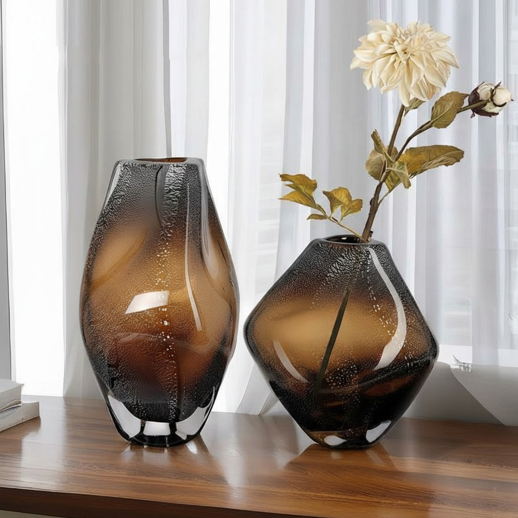 Two seeded amber glass vases on wooden table with flowers