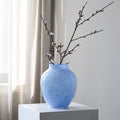 Sky blue glass vase with white speckled pattern holding cherry blossoms