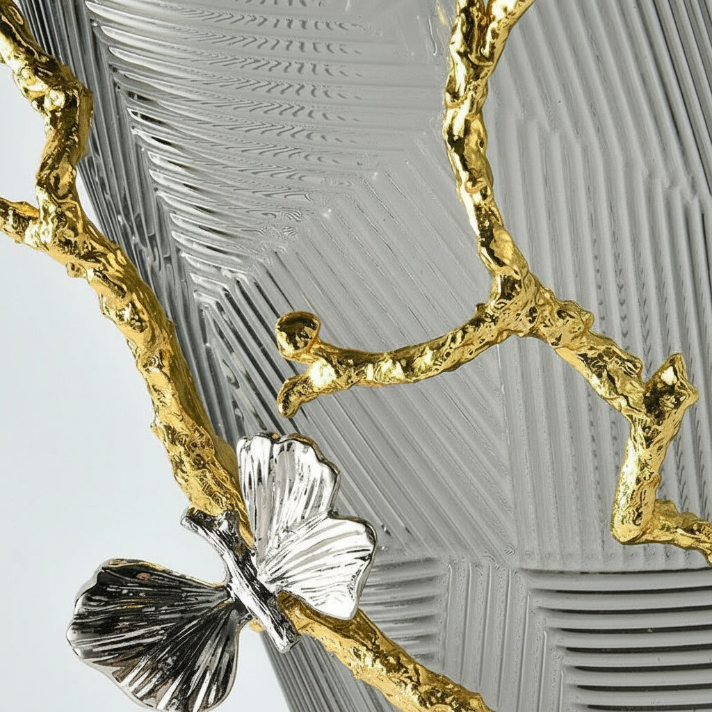 Close up detail of textured glass and sculpted gold metal branch with silver butterfly