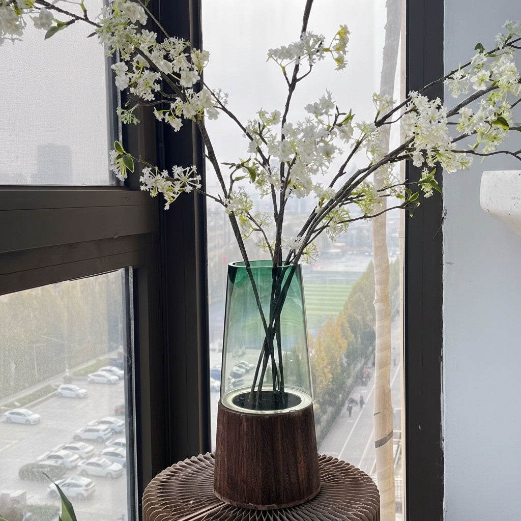 Green tinted glass vase with wood base near window