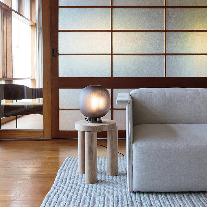 Smoked ribbed glass globe lamp on wooden stool in minimalist room