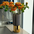 Large geometric glass vase with gold base holding orange flowers