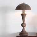 Front view of solid walnut table lamp lit against white wall