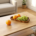 Solid wood wavy serving tray holding oranges and grapes on a table