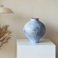 Front view of speckled blue ceramic vase on white pedestal