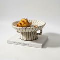 Side view of striped ceramic footed bowl with croissant