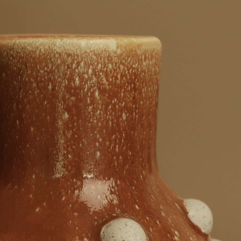 Close up detail of amber glaze and white studs on ceramic vase
