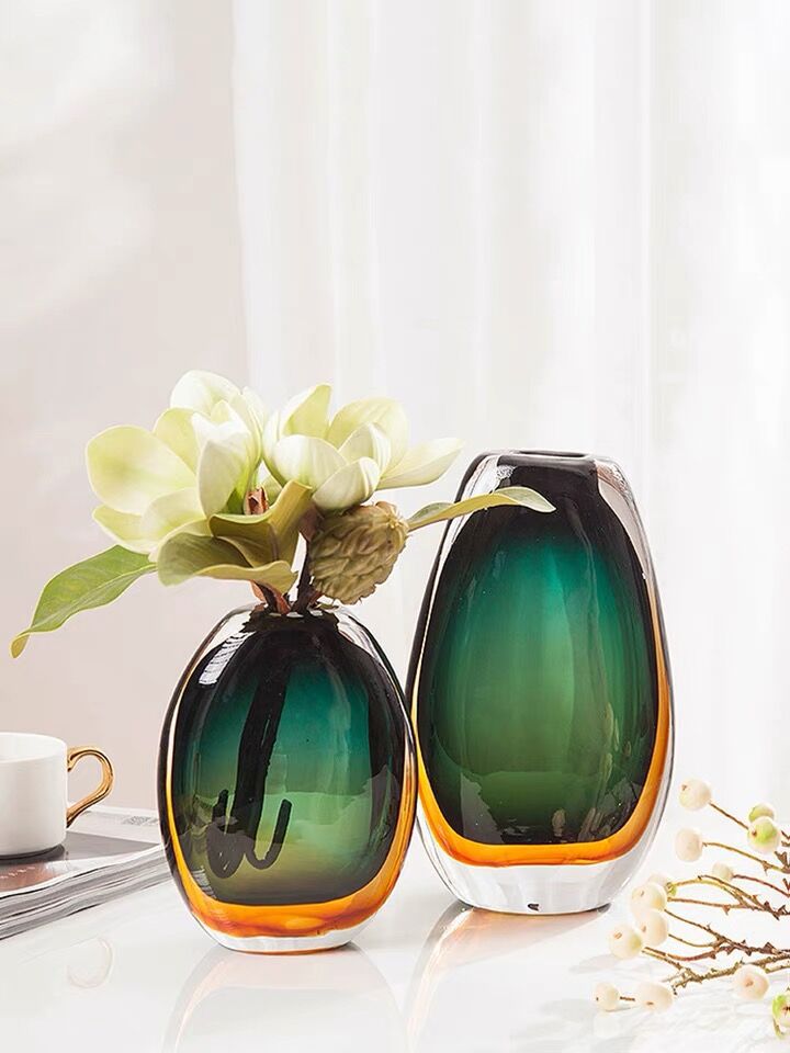 Teal and amber art glass vase with floral arrangement on table