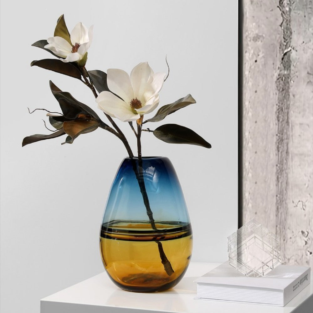 Tall teal and amber gradient glass vase styled with magnolia flowers for modern decor