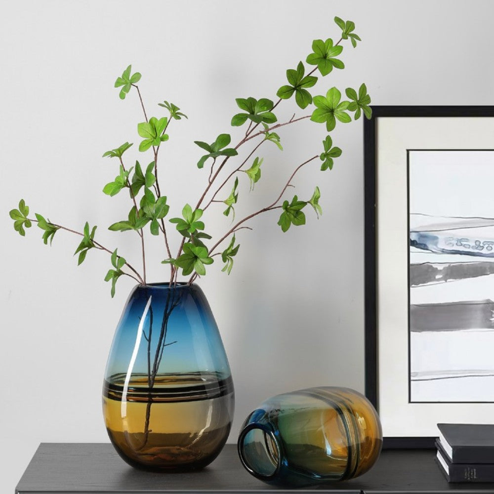 Tall and short teal amber glass vases styled with green branches in a bright interior