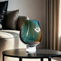 Teal and amber glass pedestal vase on a black modern coffee table.