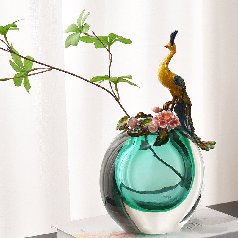 Styled teal peacock vase with green branches on table