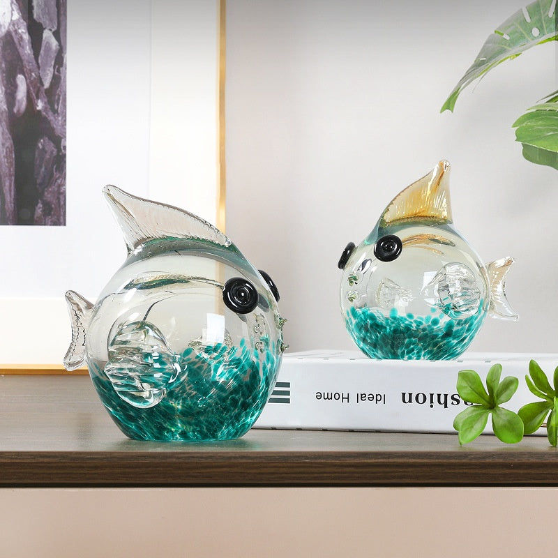Two glass fish sculptures with teal and gold detailing on a table