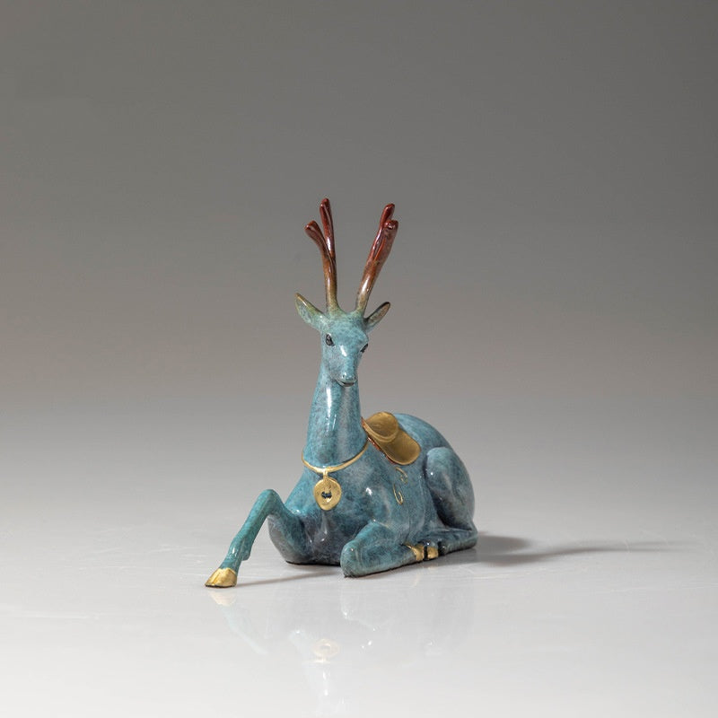 Front angle view of sitting brass deer statue with red antlers