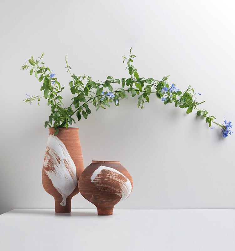 Two terracotta vases with white brushstroke accent and green foliage