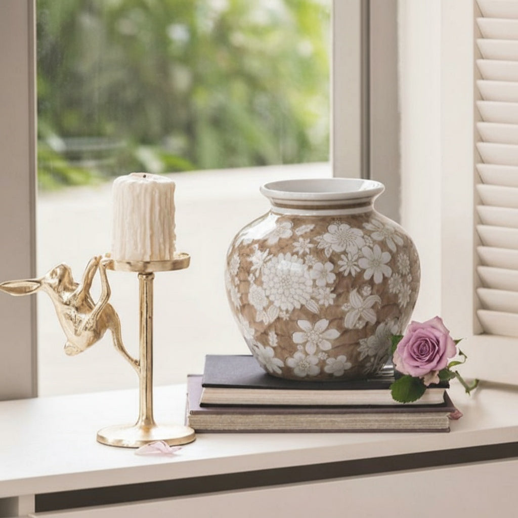 Close up of beige floral vase on window sill with gold candle holder