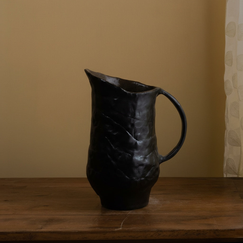 Angled view of textured black ceramic pitcher on wooden table
