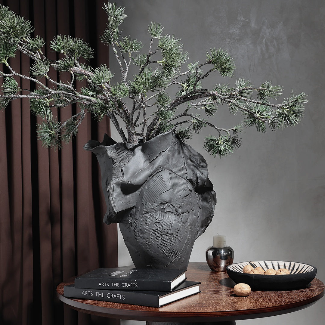 Textured black ceramic vase with pine branches on table