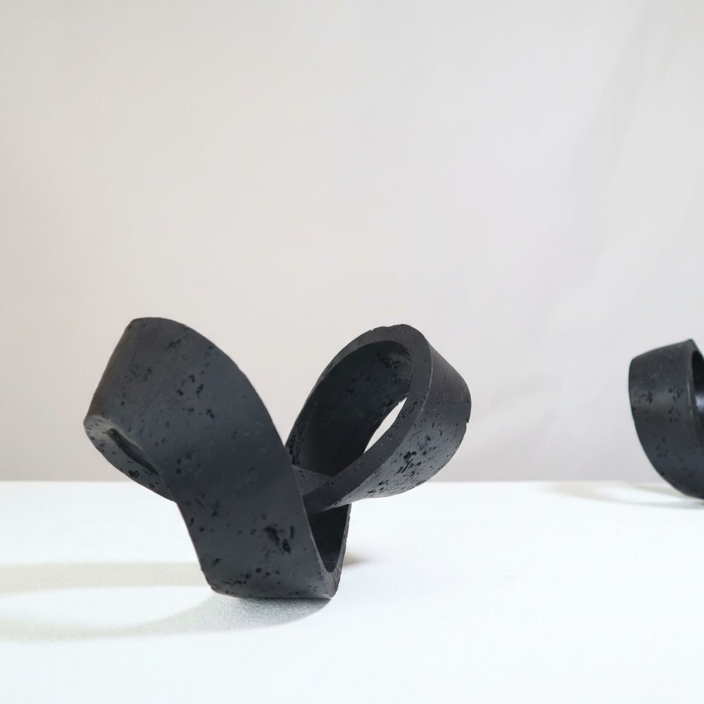 Textured black concrete abstract knot sculpture on white surface