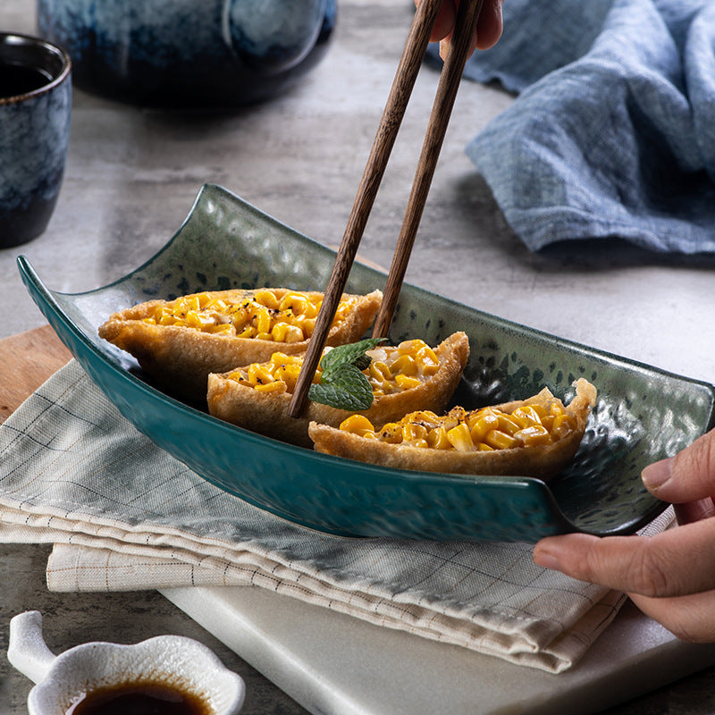 Close up of deep teal curved ceramic platter holding corn sushi with chopsticks